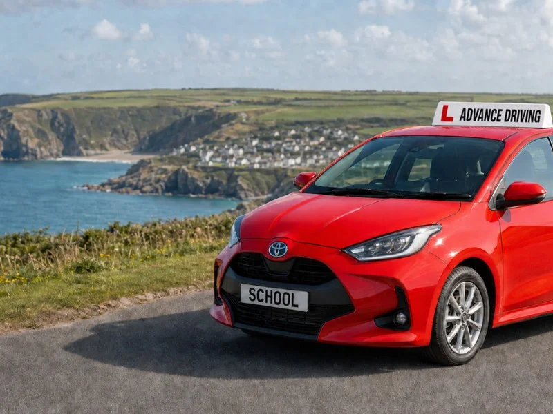 Advance Driving school red Toyota Yaris car parked on a Cornish coastal road overlooking the sea